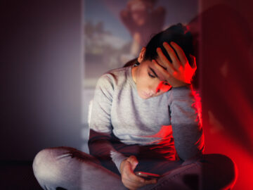 How to protect yourself from online harassment A 13-year-old girl is using her smartphone in the dark room. The content she is browsing projects in front of her.